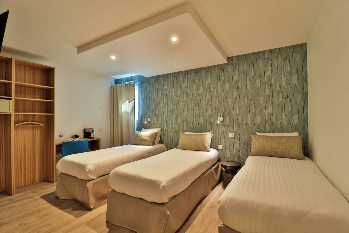 A hotel room with two single beds, a desk with a chair, a wardrobe, and a shower area.
