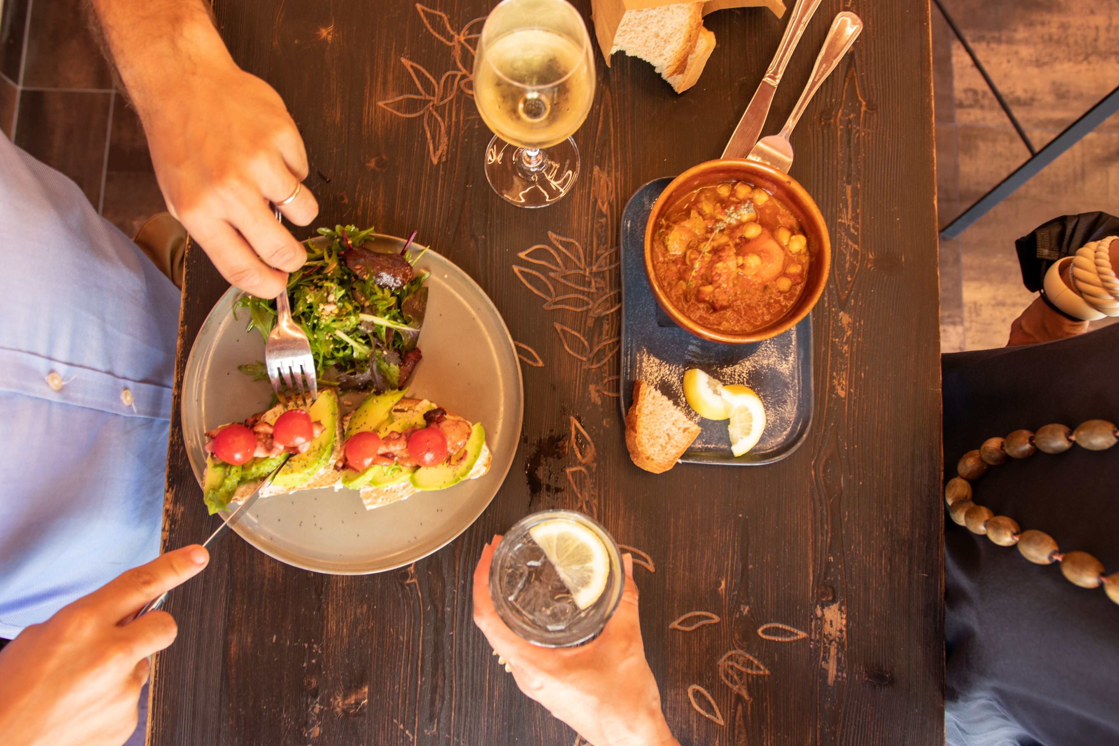 A dining table with a plate of food, a bowl of soup, a glass of white wine, and a glass of water.