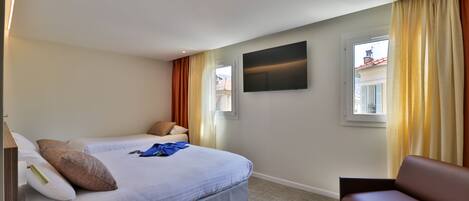 A hotel room with two beds, a flat-screen TV, a sofa, and a window with curtains.