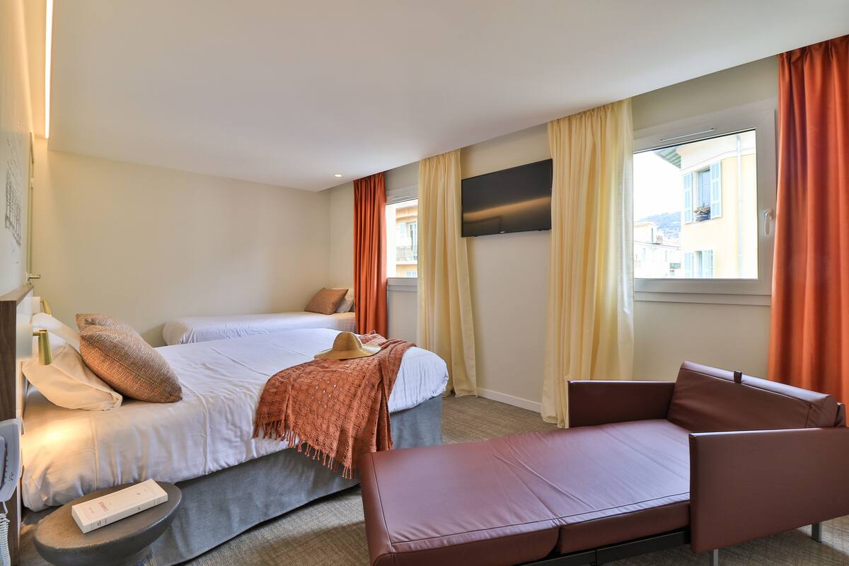 A hotel room with a bed, a sofa, a TV, and a window with curtains.