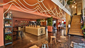 Um interior moderno com área de bar central, assentos de madeira e uma escadaria que leva a um andar superior.