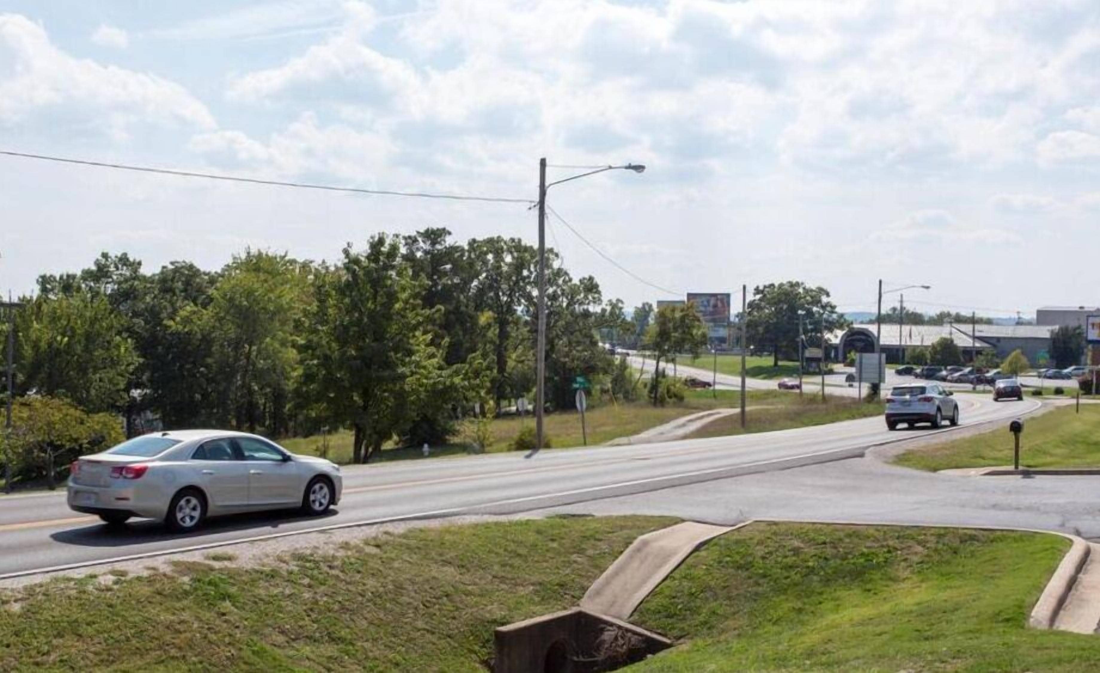 A road intersection with cars, a grassy median, and trees.