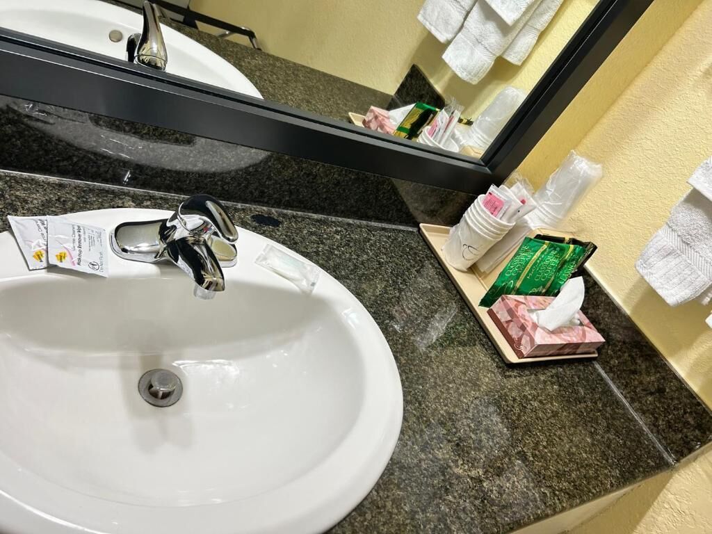 A white sink with a chrome faucet, a mirror above it, and a countertop with toiletries and a tissue box.