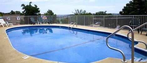 Une piscine extérieure dotée d’une rambarde en métal, entourée d’une clôture et de chaises.