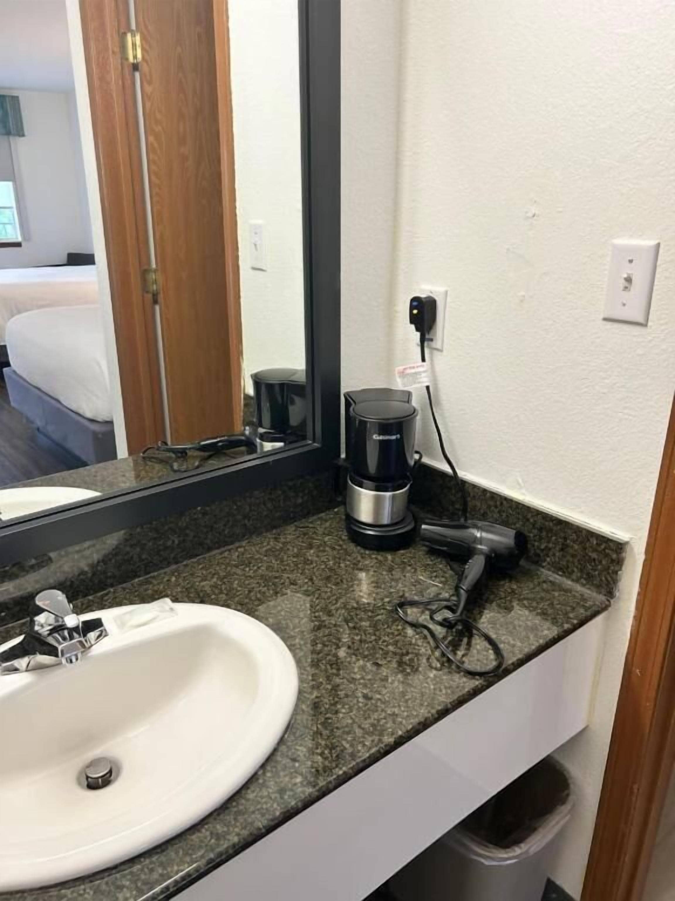 A hotel bathroom with a white sink, a mirror, a coffee maker, and a hairdryer.
