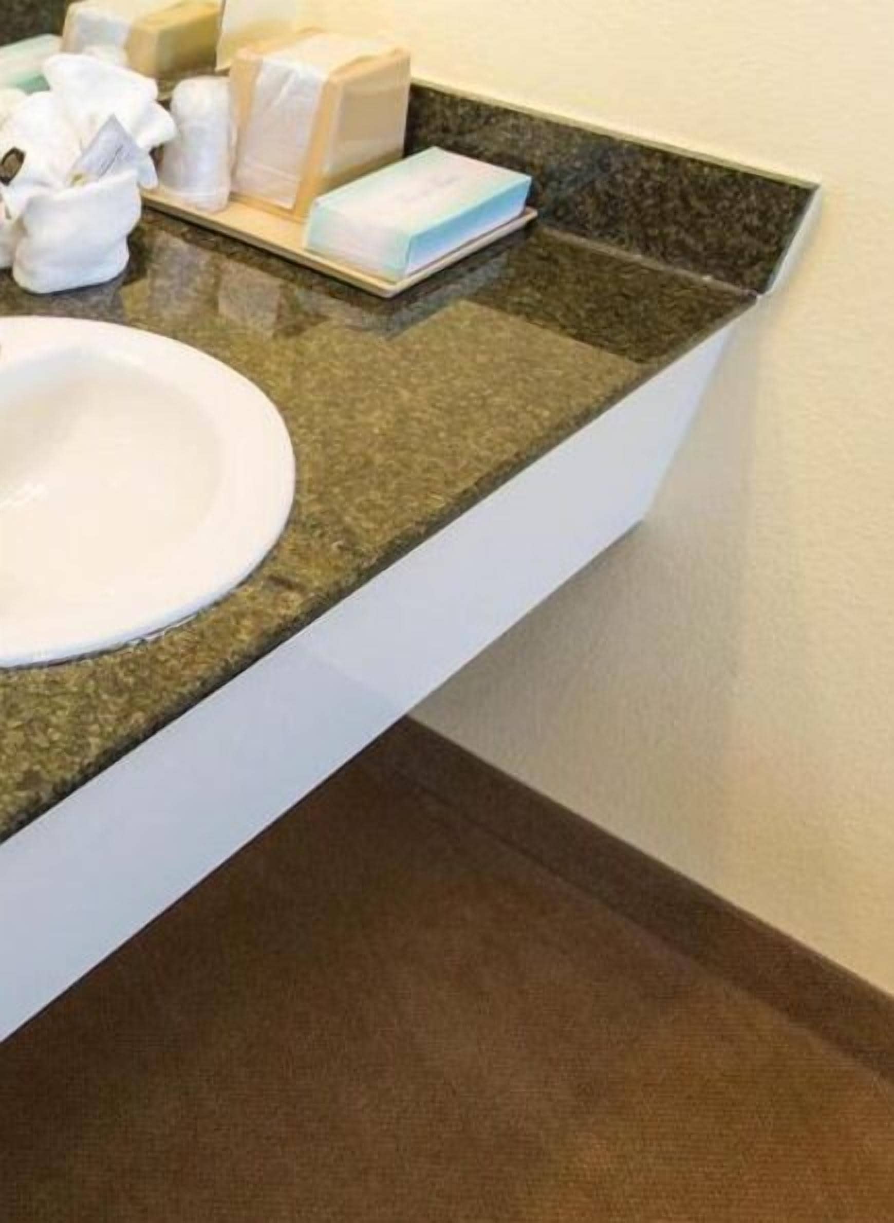 A bathroom with a granite countertop, a white sink, and toiletries.