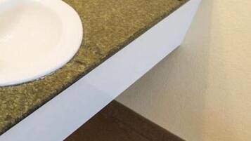 A bathroom with a granite countertop, a white sink, and toiletries.