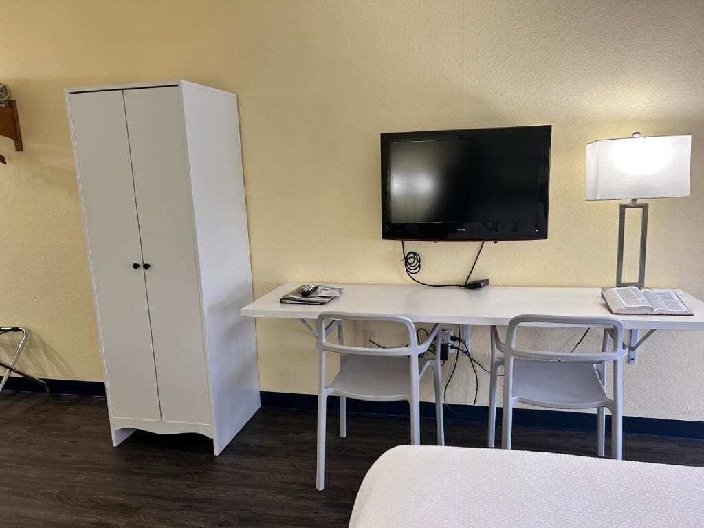 Una habitación de hotel con cama, escritorio con televisor, lámpara y armario.
