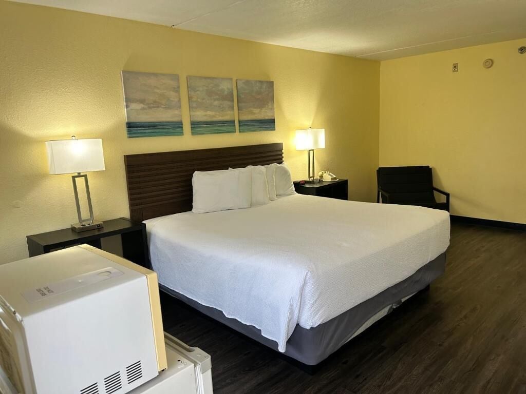 A hotel room with a large bed, two bedside lamps, a nightstand, a chair, and a wall-mounted phone.