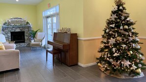 Ein Wohnzimmer mit Kamin, Klavier, Weihnachtstannen und einer Tür zu einem anderen Raum.