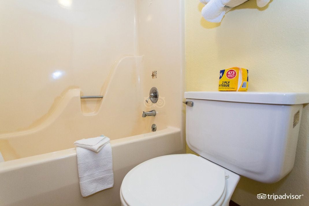A bathroom with a bathtub, toilet, and a shelf with a box of toilet paper.