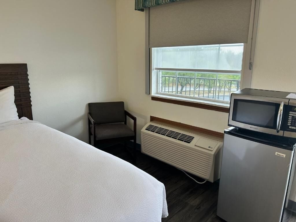 Una habitación de hotel con una cama, una silla, un microondas y un refrigerador.