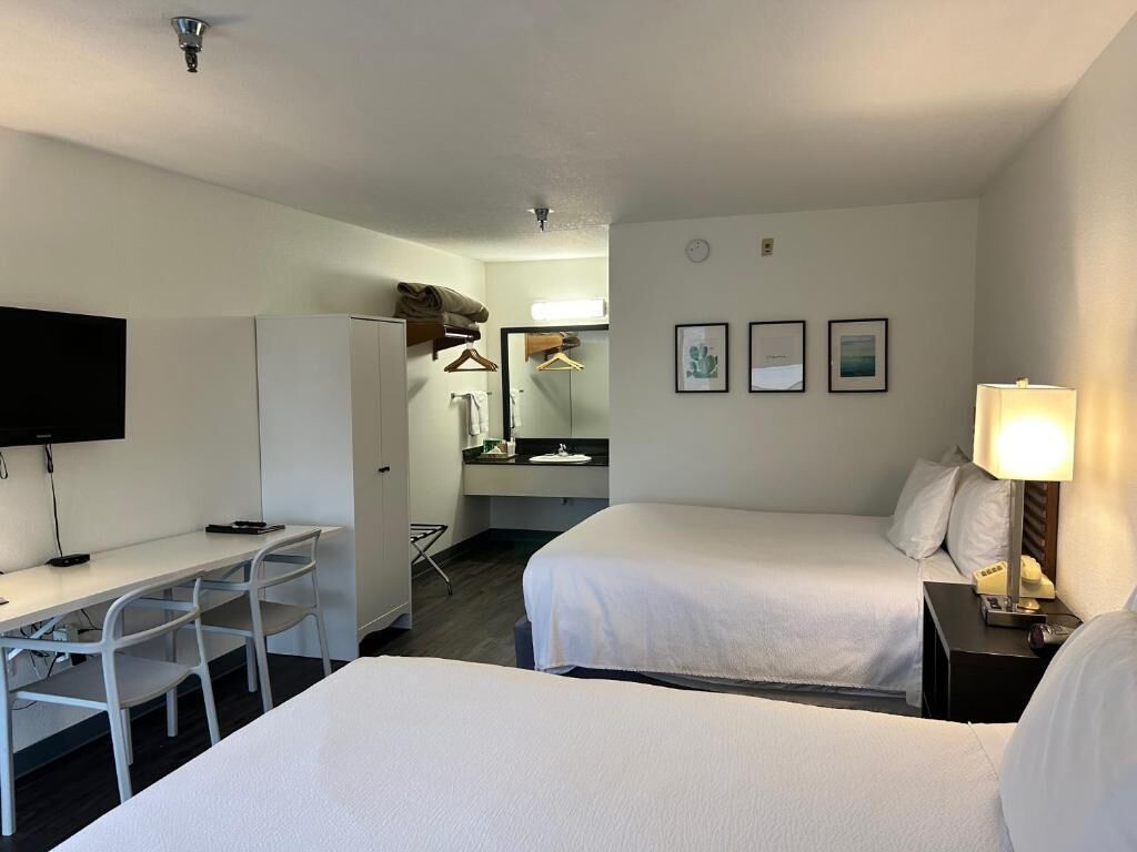 A hotel room with two beds, a desk with a chair, a television, and a mirror.