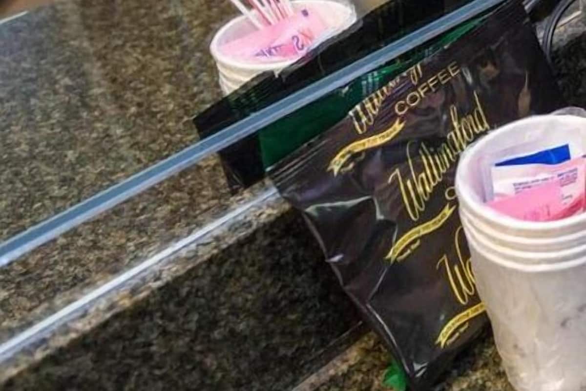 A coffee machine, a packet of coffee creamer, and a cup with a spoon on a granite countertop.