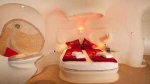 Un dormitorio de diseño único con un muro de mosaico circular, una cama con ropa de cama roja y una lámpara moderna sobre la cama.