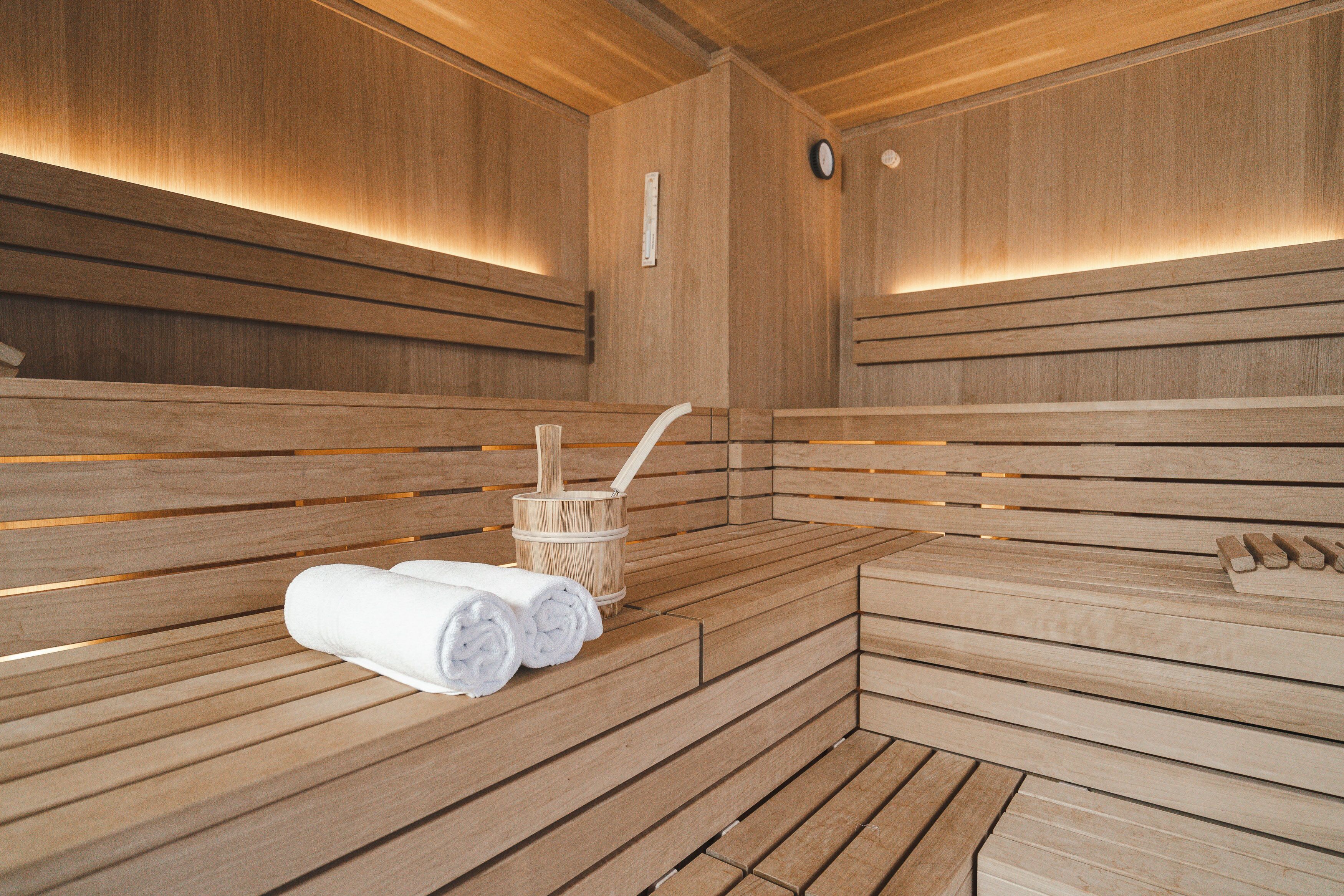 Een houten sauna met banken, een houten emmer en opgerolde handdoeken.