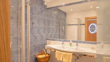 A bathroom with a glass shower enclosure, a sink with a mirror, and a wicker basket with towels.