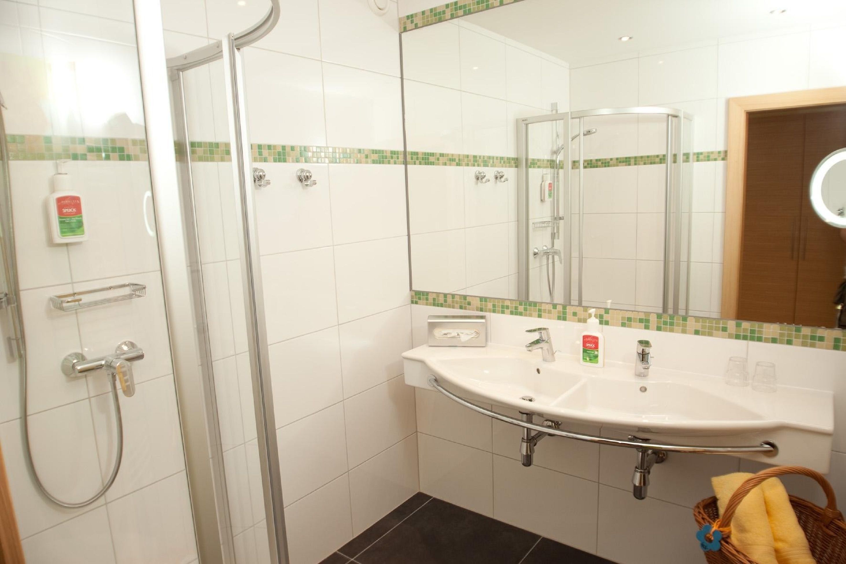 A bathroom with a glass shower enclosure, a white sink with a mirror above it, and a small basket with towels.