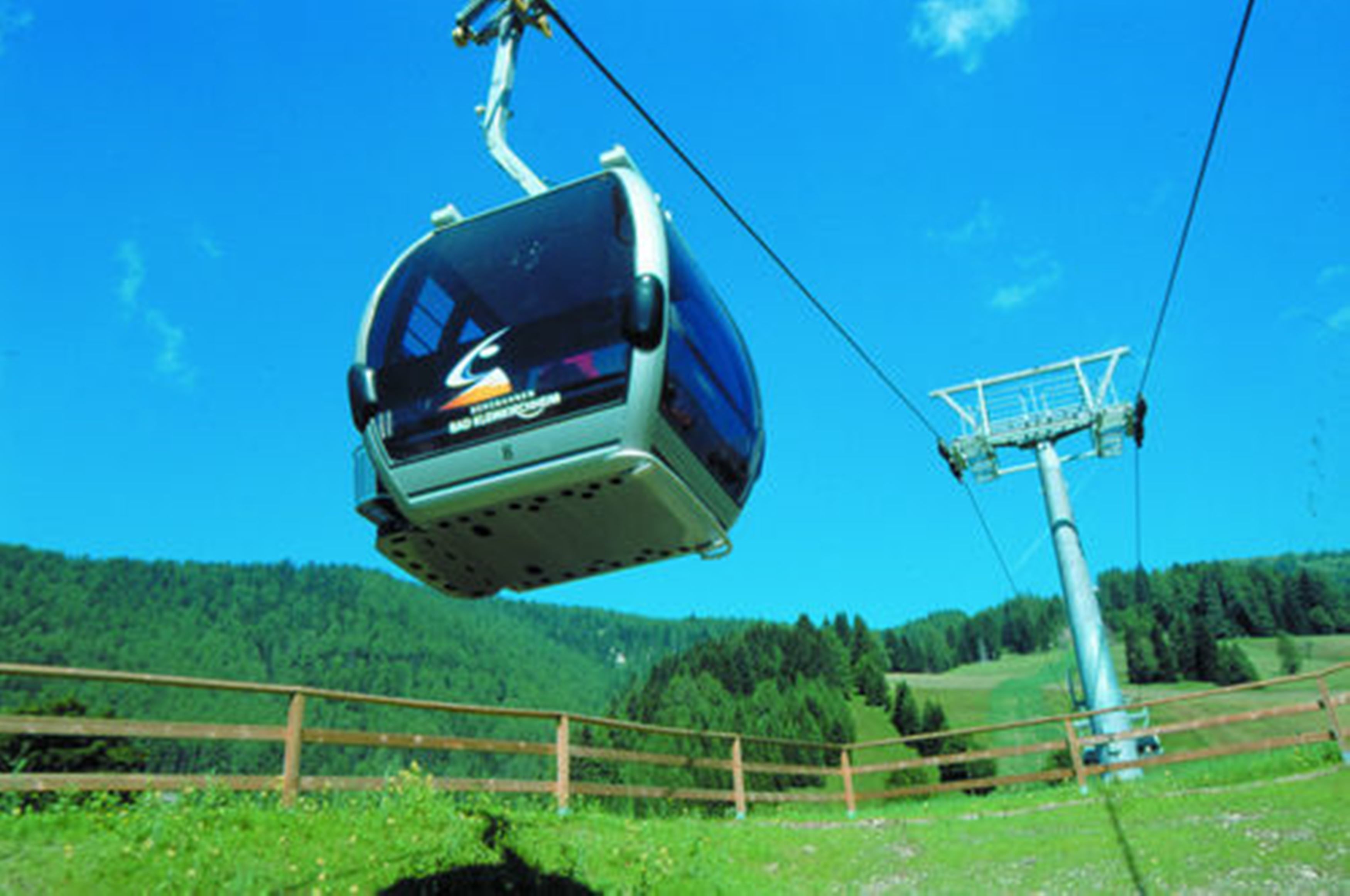 A cable car in motion, suspended by cables, with a mountainous landscape in the background.