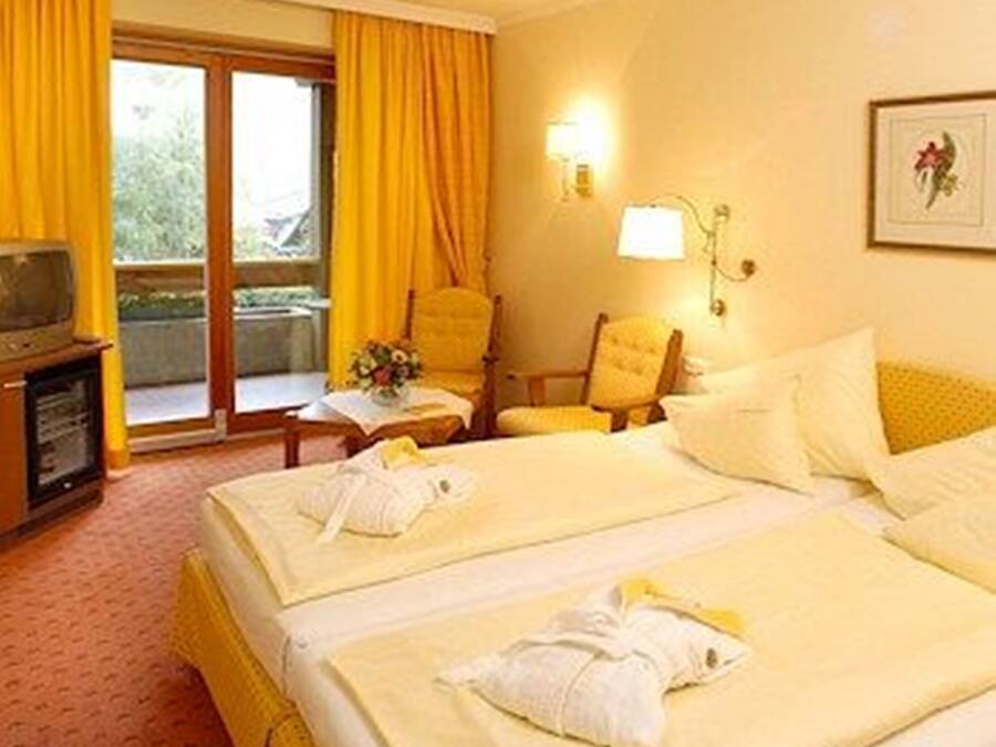 Habitació d'hotel amb dos llits, un escriptori, una cadira, un televisor i una finestra amb cortines.