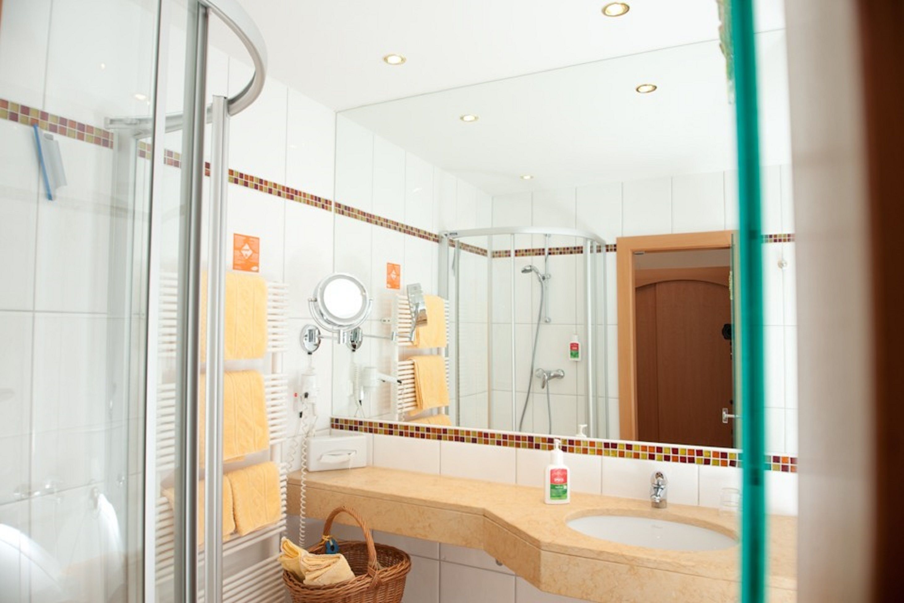 Ein Badezimmer mit Duschkabine aus Glas, Waschbecken mit Spiegel und Handtuchhalter mit gelben Handtüchern.