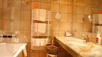Um banheiro com banheira, pia com bancada de mármore, porta-toalhas com várias toalhas, espelho redondo e um cesto decorativo.