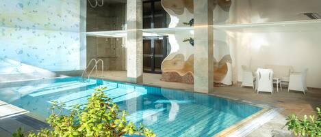 An indoor swimming pool with clear water, surrounded by stone walls and modern furniture.