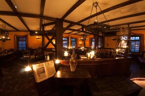 Un restaurante tenuemente iluminado con vigas de madera y faroles colgantes, mesas con velas y un menú sobre la mesa.