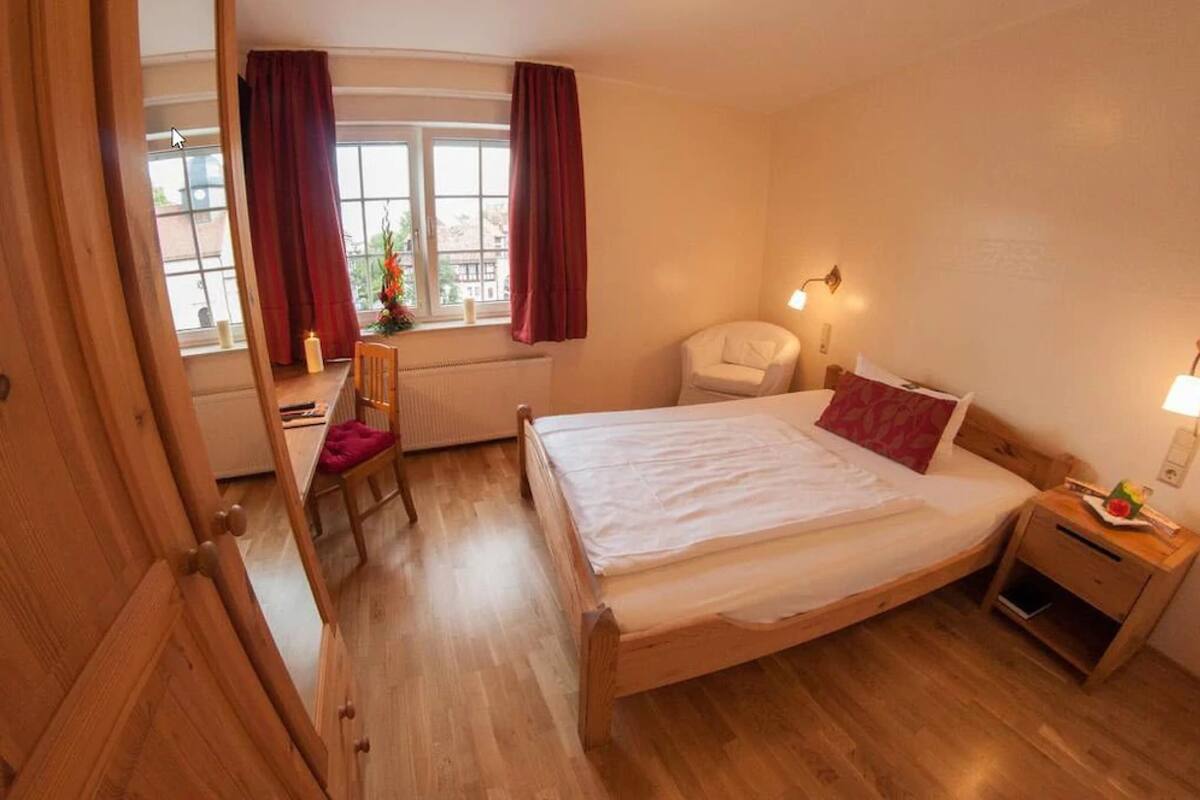 Une chambre à coucher avec un lit en bois, une chaise, un bureau et une fenêtre avec des rideaux.