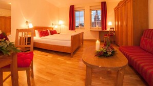A cozy hotel room with a wooden bed, a small table with flowers, a sofa, and a view of a building through the window. - Lutherhotel Eisenacher Hof - Ringhotel (Eisenach)