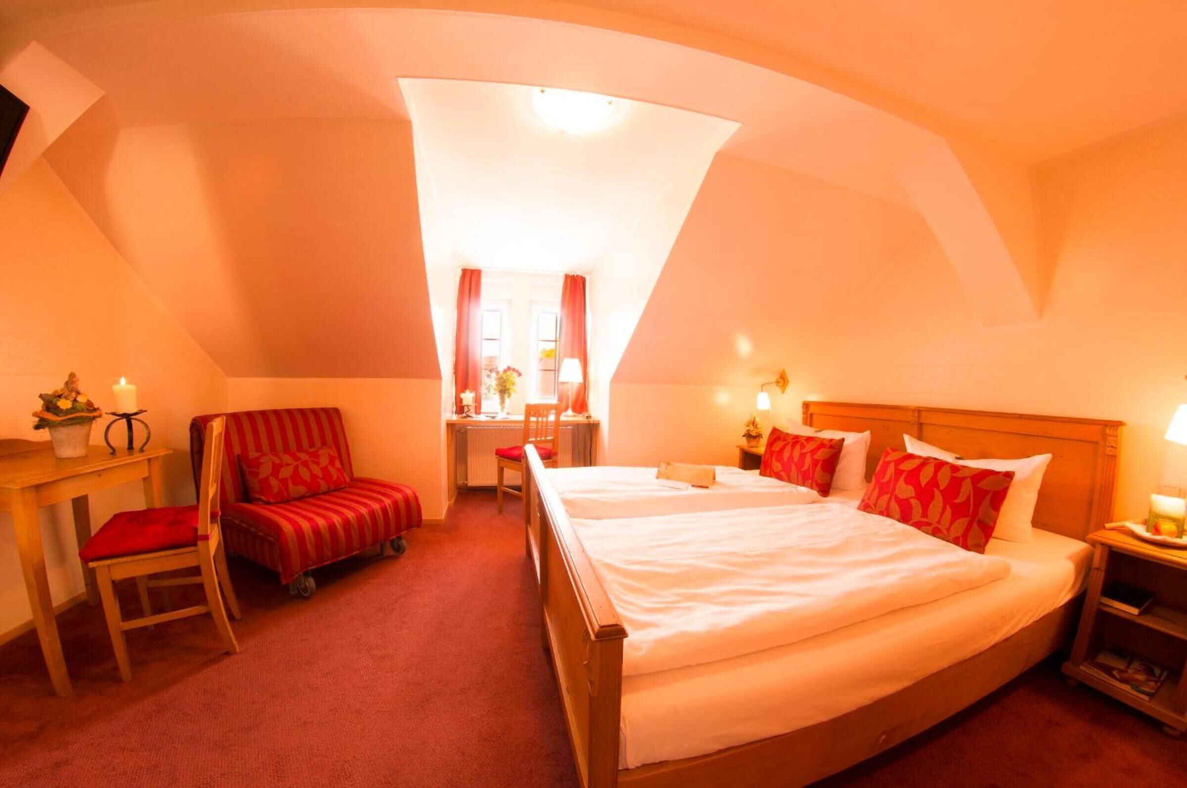 A bedroom with a large bed, a desk, a chair, and a small table with a lamp.