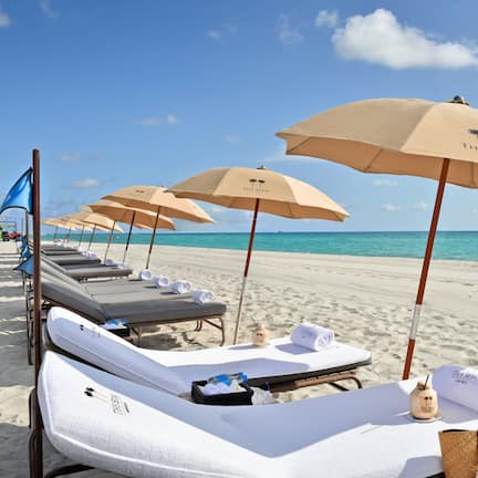 A beachside hotel with sun loungers, beige umbrellas, and a clear view of the ocean.