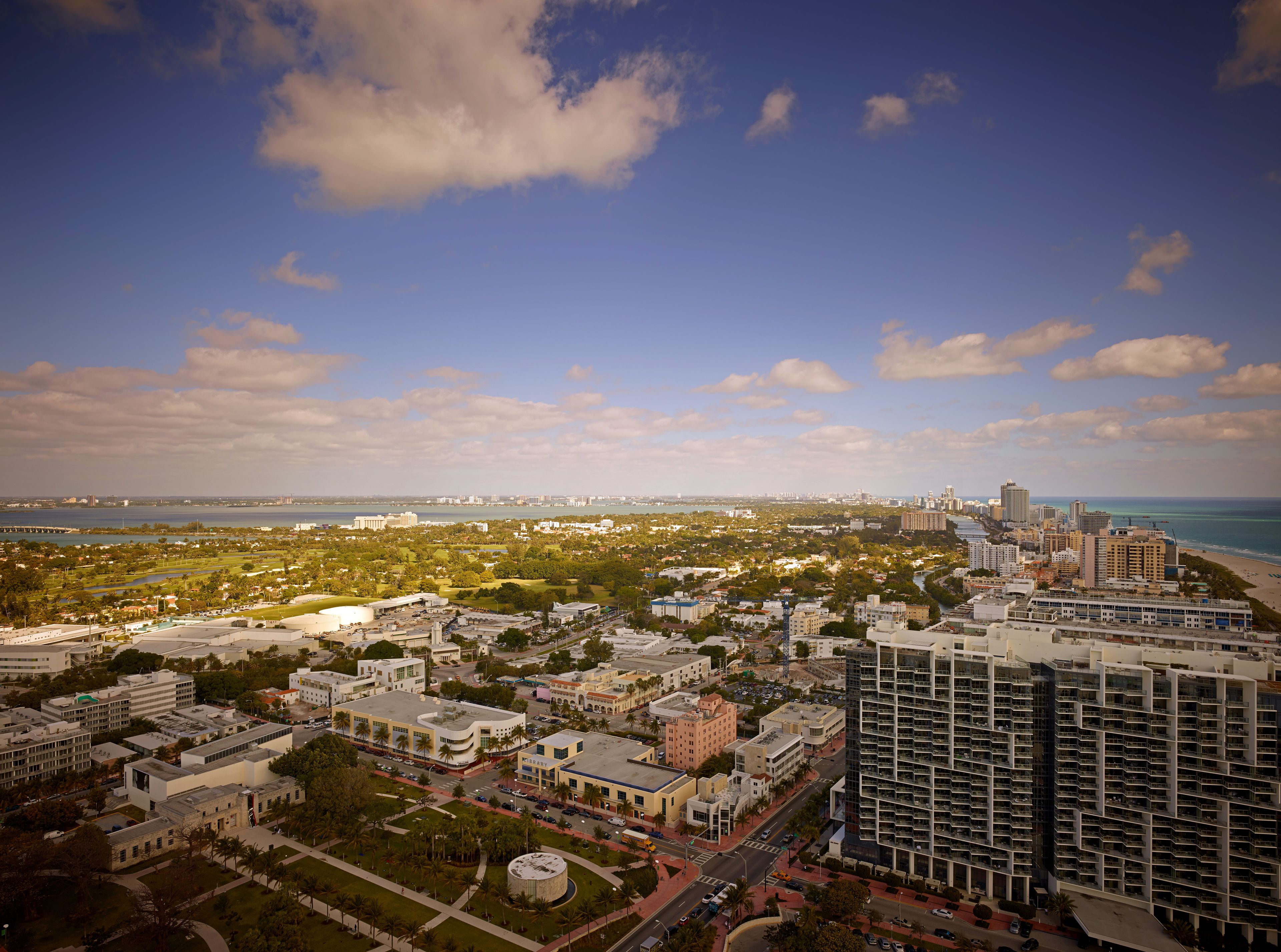 A high-rise building with a modern architectural design, surrounded by a mix of commercial and residential buildings, and a view of the coastline in the background.