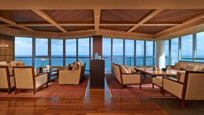 A spacious living area with a high ceiling, large windows offering a view of the ocean, and modern furniture.