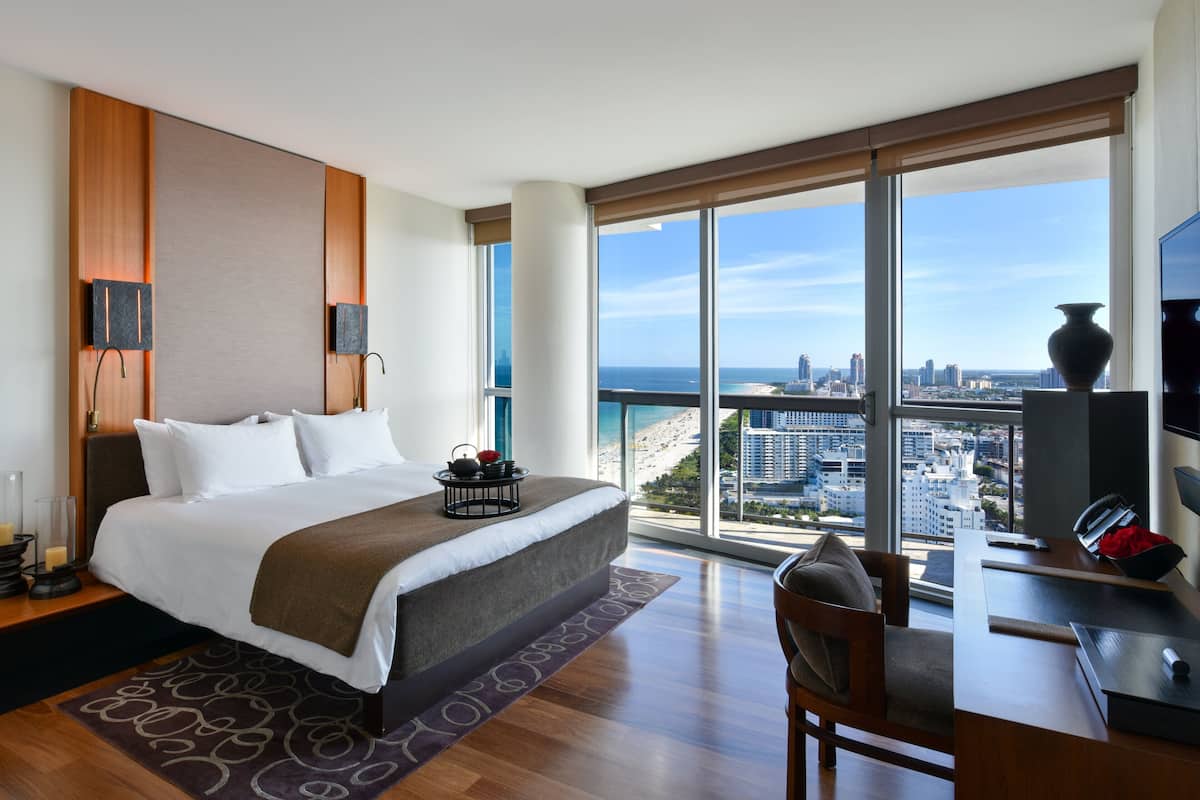 Ein modernes Hotelzimmer mit einem großen Bett, einem Schreibtisch und Blick auf Stadt und Meer.