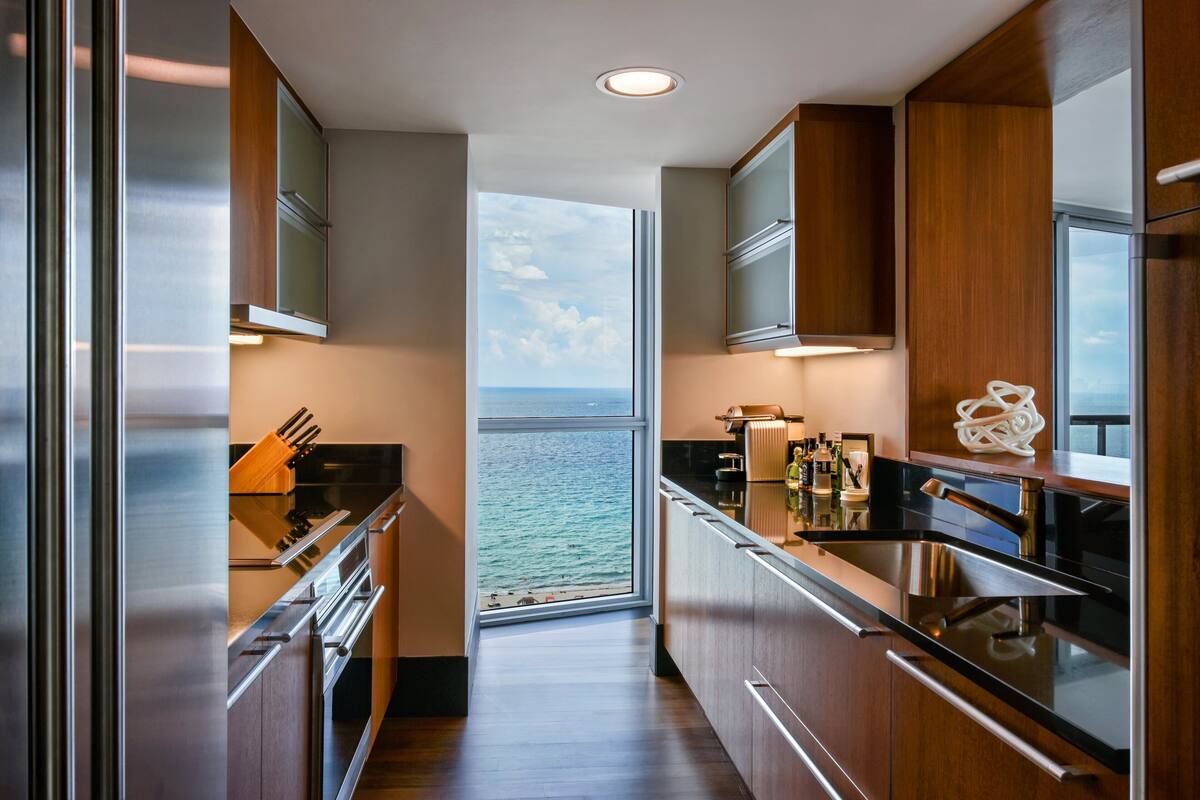 A modern kitchen with stainless steel appliances, wooden cabinets, and a view of the ocean.
