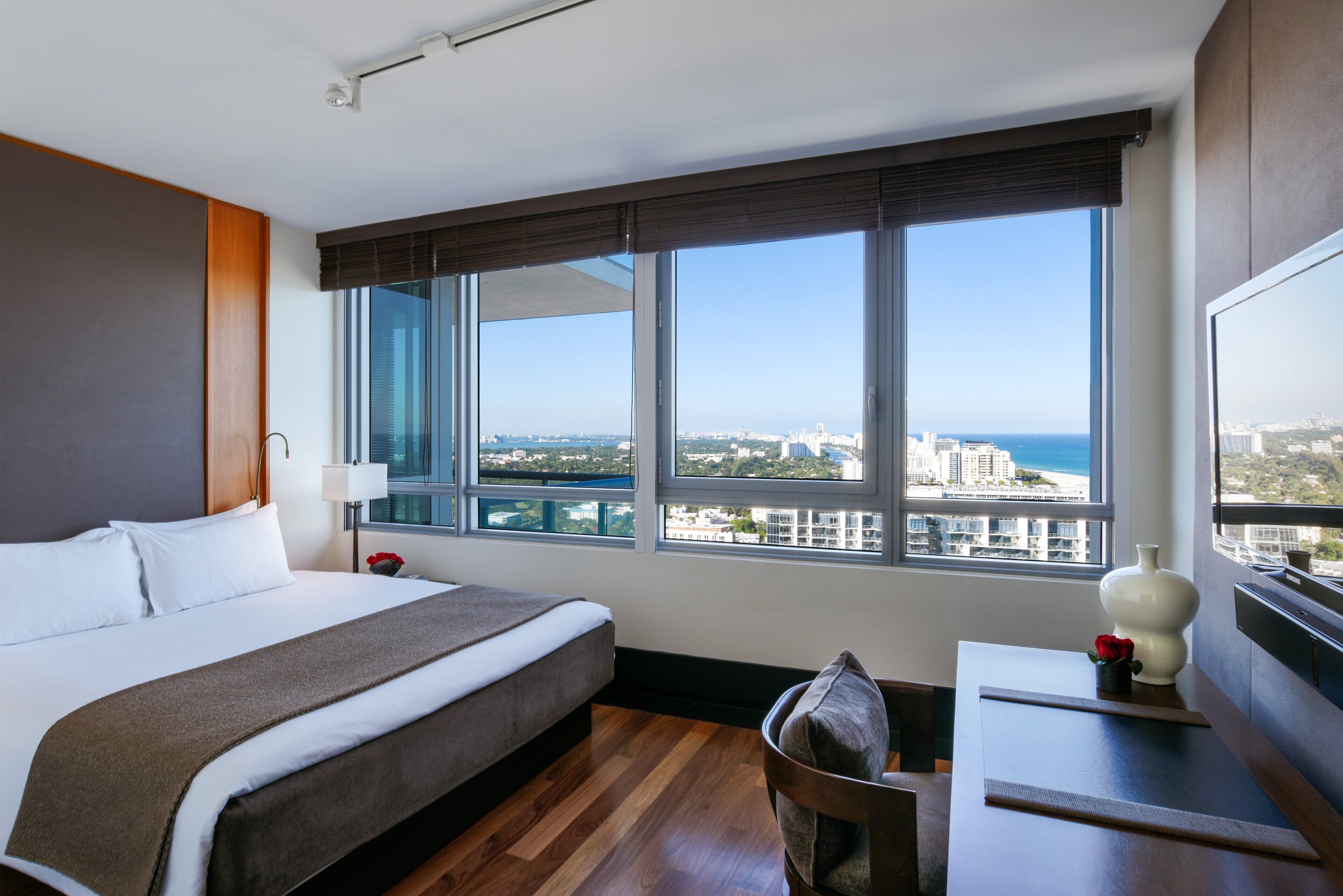 Habitación de hotel con una cama grande, un escritorio y vistas a la ciudad y al océano.