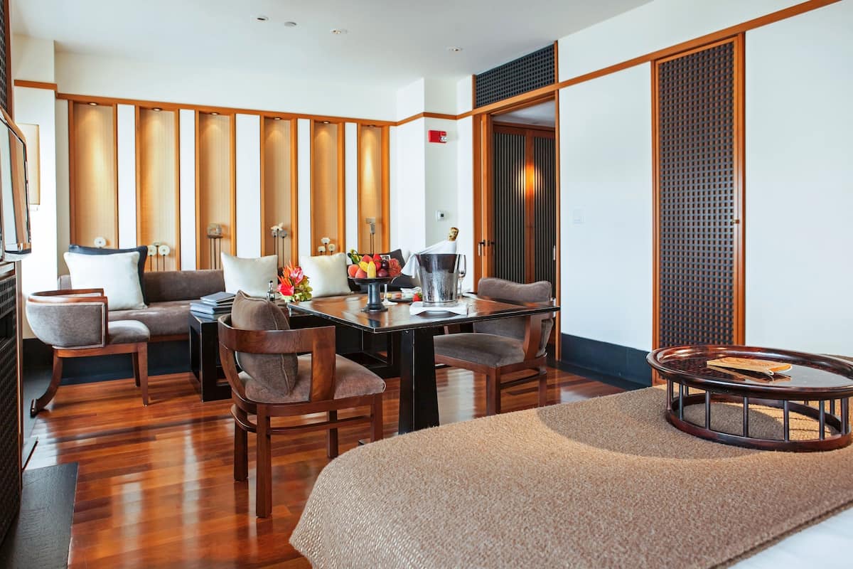 Ein modernes Hotelzimmer mit Holzboden, einer Sofagarnitur, einem Esstisch und einem kleinen runden Tisch.