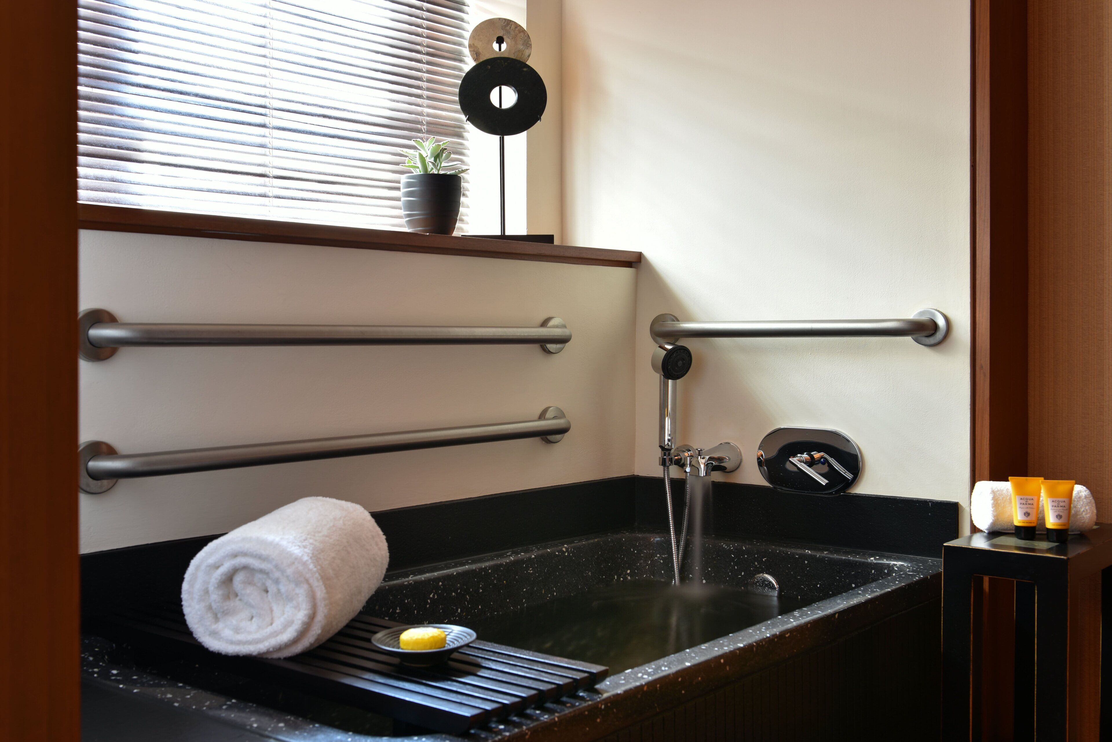 A bathroom with a black sink, towel rack, and a small potted plant on the window sill.