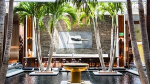 A pool area with a central fountain, surrounded by palm trees and seating areas.
