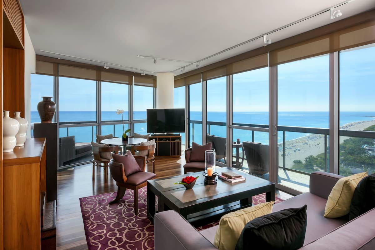 Ein geräumiges Wohnzimmer mit großem Fenster und Meerblick, ausgestattet mit einer Couch, Sesseln und einem Couchtisch.