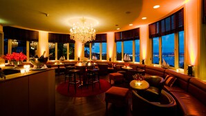 Ein großzügiger Lounge-Bereich mit einer zentralen Bar, bequemen Sitzgelegenheiten und großen Fenstern mit Blick aufs Wasser.