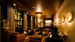 Ein gut beleuchteter Lounge-Bereich mit Ledersofas, einer Bar und großen Fenstern mit Vorhängen.