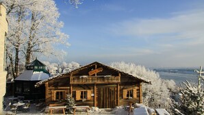 Eine Holzchalet mit Balkon, umgeben von schneebedeckten Bäumen und Blick auf einen Fluss.