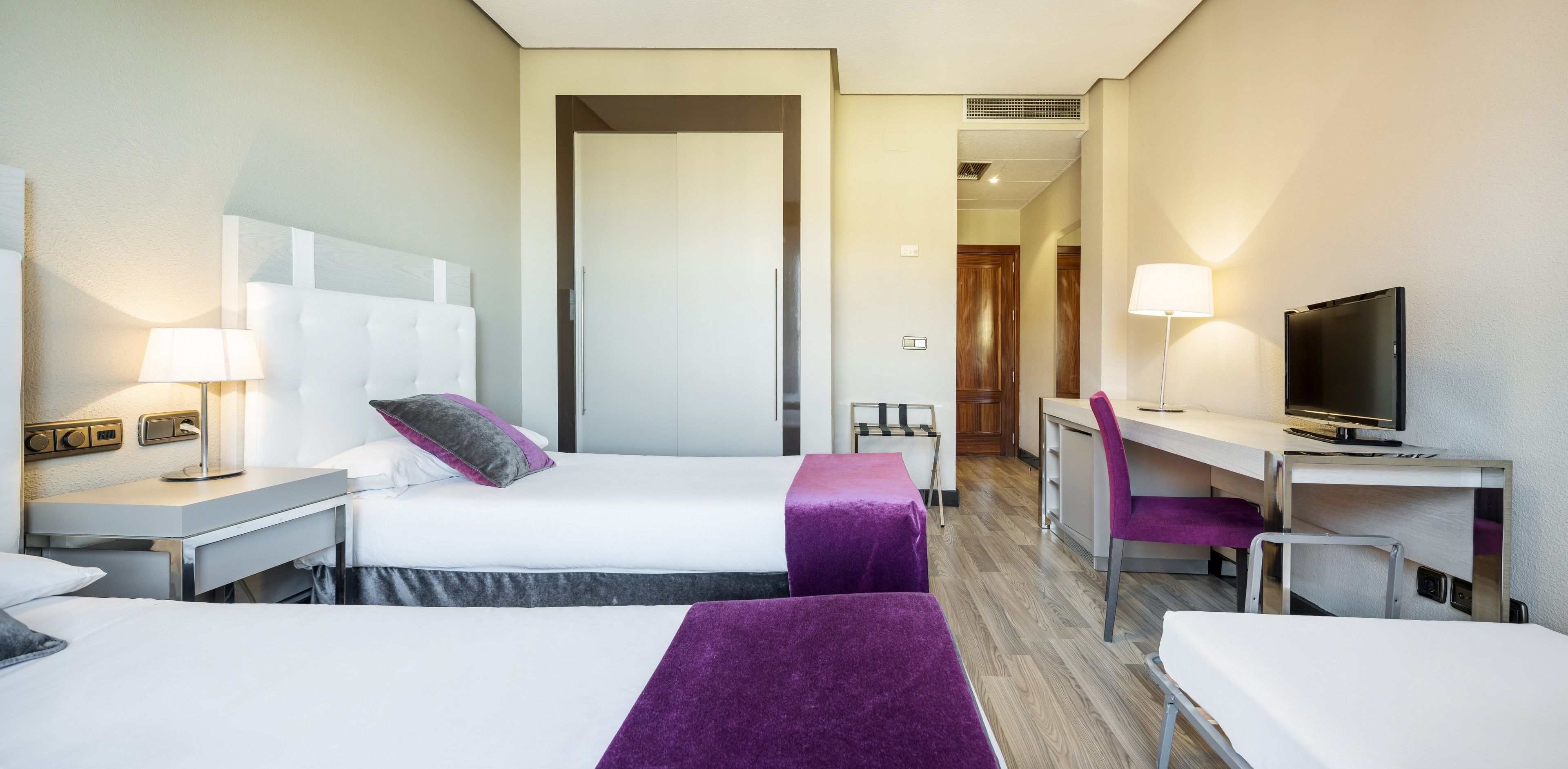 Habitación de hotel con dos camas, un escritorio, un televisor y una lámpara.