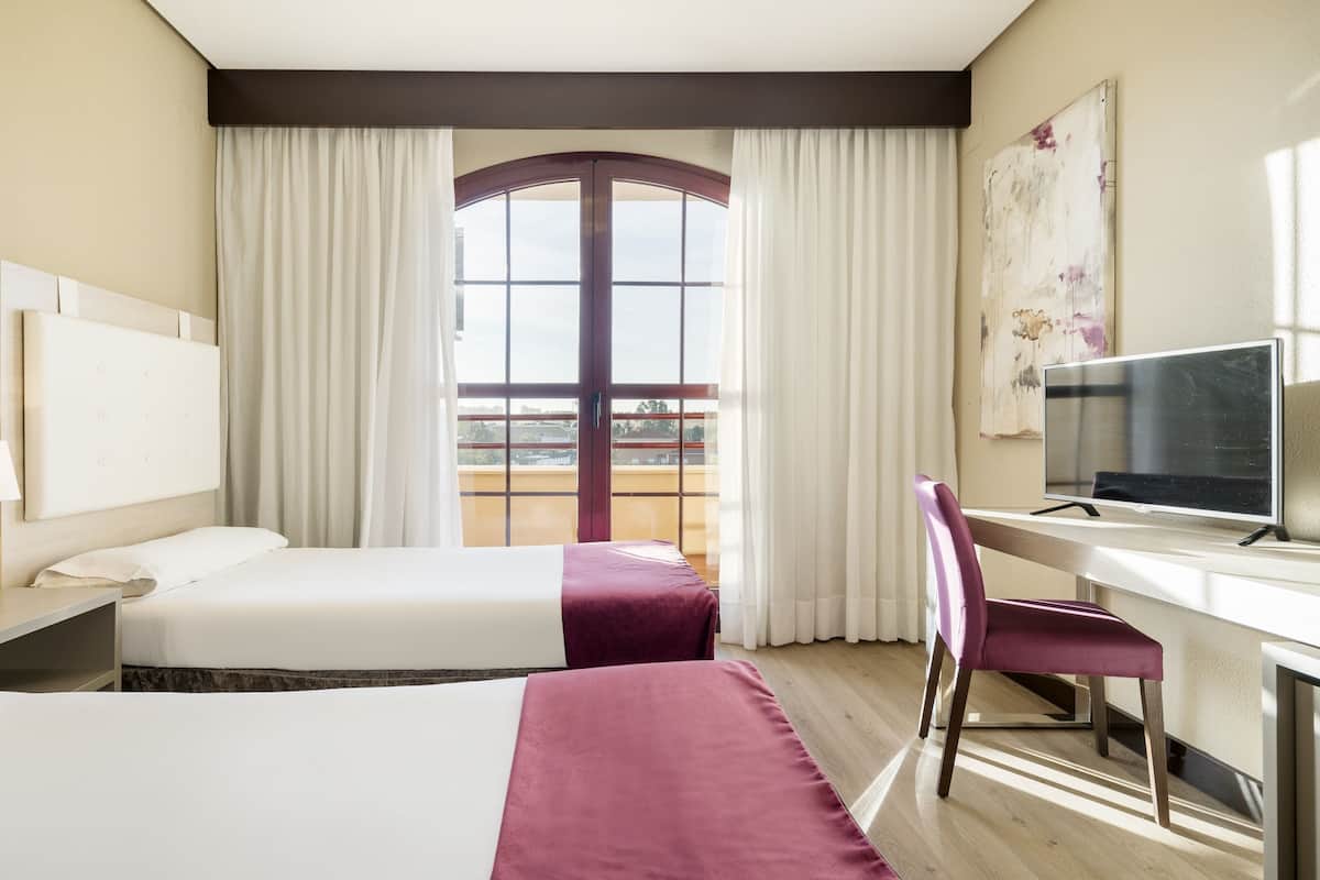 A hotel room with two beds, a desk with a TV, a chair, and a window with curtains.