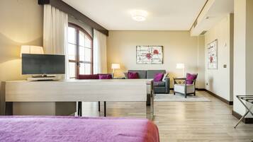 Ein Hotelzimmer mit Bett, Schreibtisch, Fernseher, Sofa und Sessel.