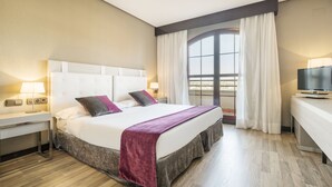 A hotel room with a large bed, bedside tables, a desk, a television, and a window with curtains. - Hotel ILUNION Golf Badajoz (Badajoz)