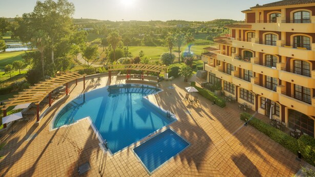 A hotel with a pool, outdoor seating, and a view of the surrounding landscape. - Hotel ILUNION Golf Badajoz (Badajoz)