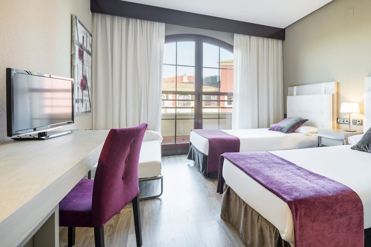 A hotel room with two beds, a desk, and a TV.